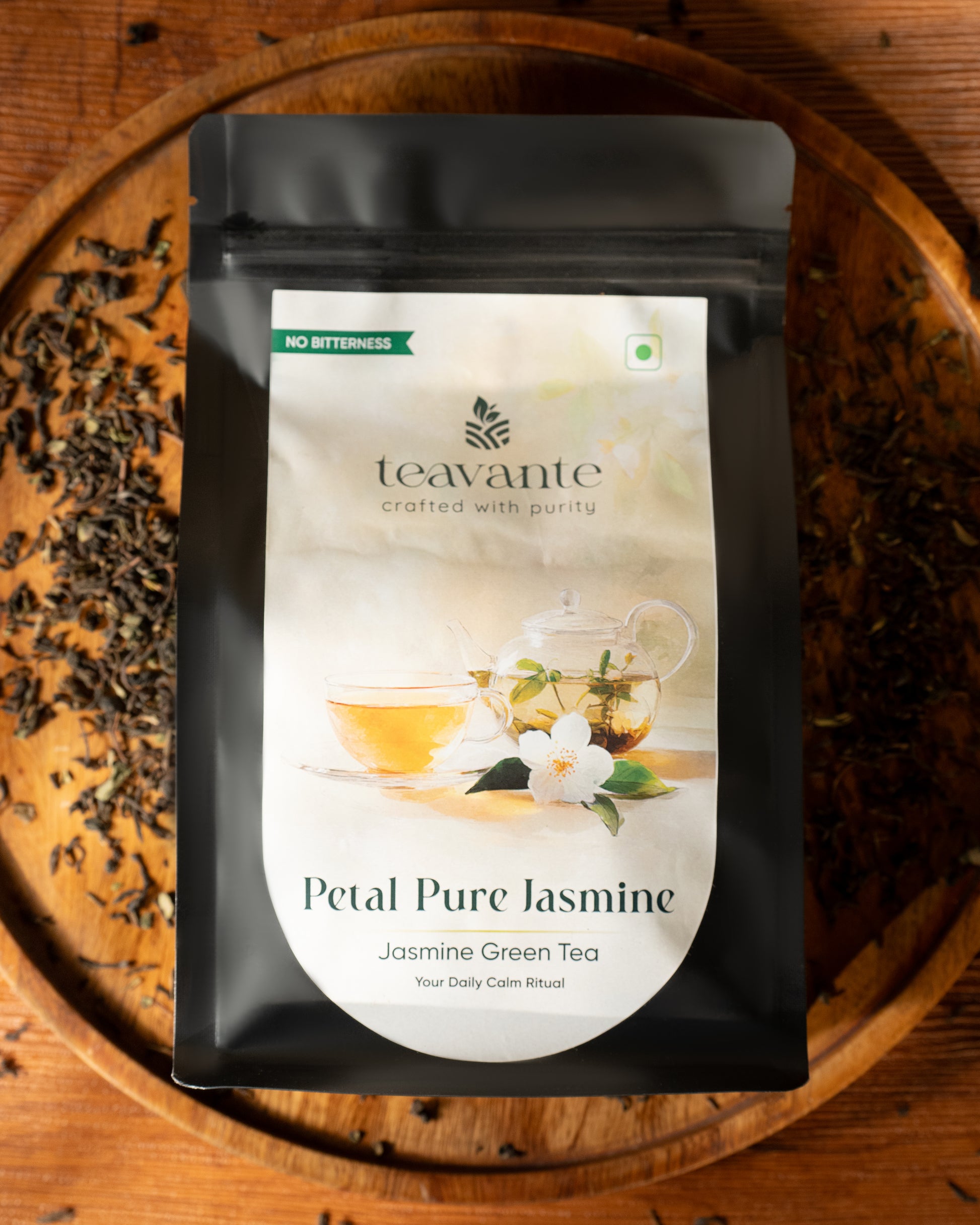 A stand-up pouch of Teavante Petal Pure Jasmine Jasmine Green Tea, placed on a round wooden tray with loose tea leaves scattered around it.